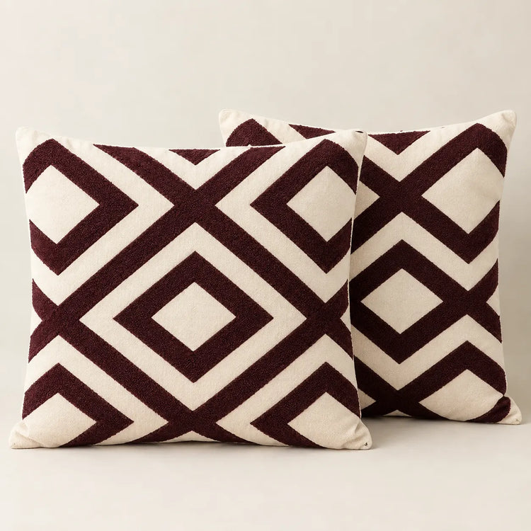 Two cream cushion covers with bold burgundy interlocking diamond patterns on a sofa.