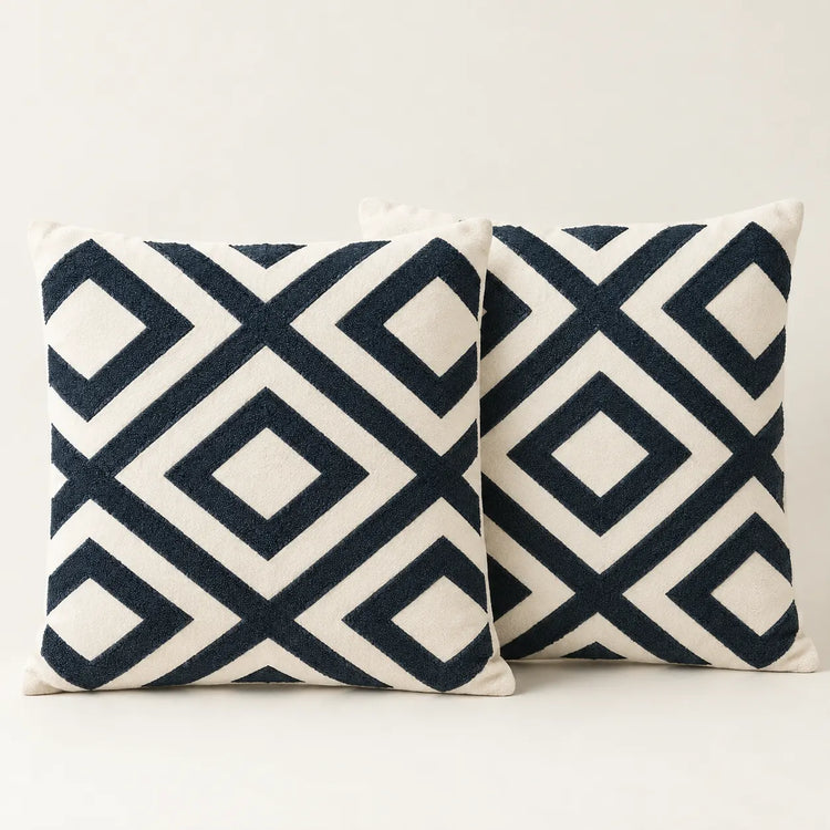 Two cream cushion covers with bold navy interlocking diamond patterns on a sofa.