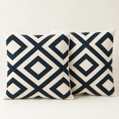Two cream cushion covers with bold navy interlocking diamond patterns on a sofa.