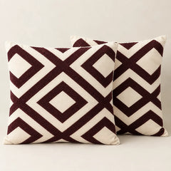 Two cream cushion covers with bold burgundy interlocking diamond patterns on a sofa.