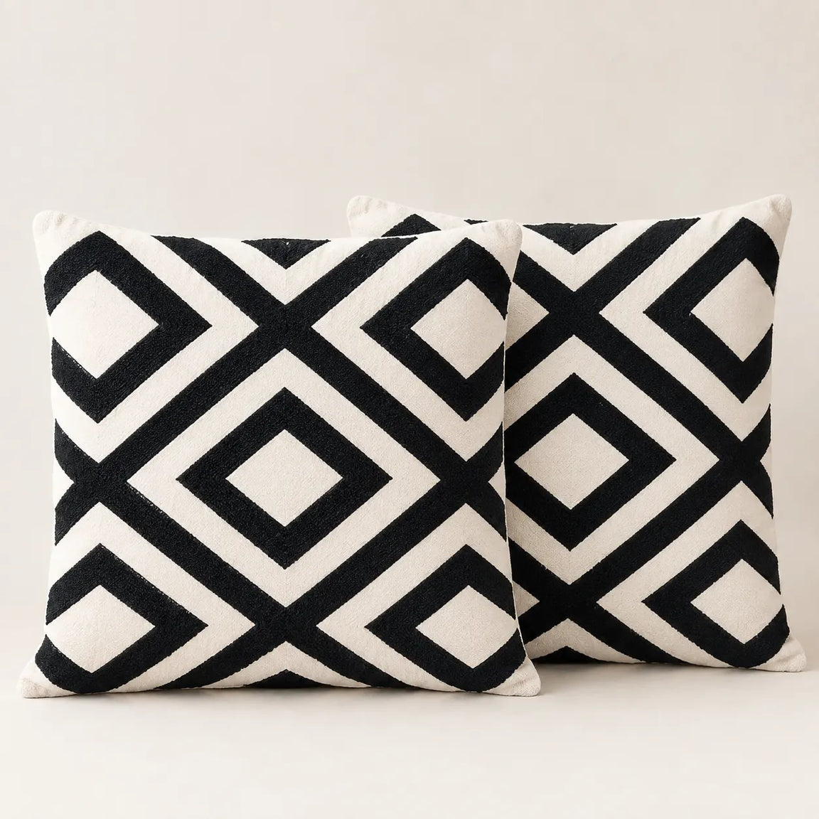 Two cream cushion covers with bold black interlocking diamond patterns on a sofa.