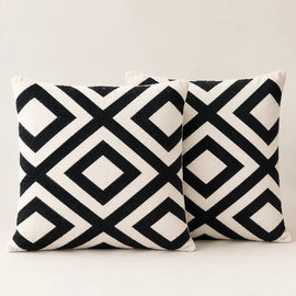 Two cream cushion covers with bold black interlocking diamond patterns on a sofa.