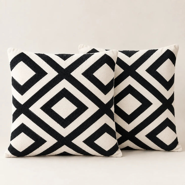 Two cream cushion covers with bold black interlocking diamond patterns on a sofa.