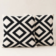 Two cream cushion covers with bold black interlocking diamond patterns on a sofa.