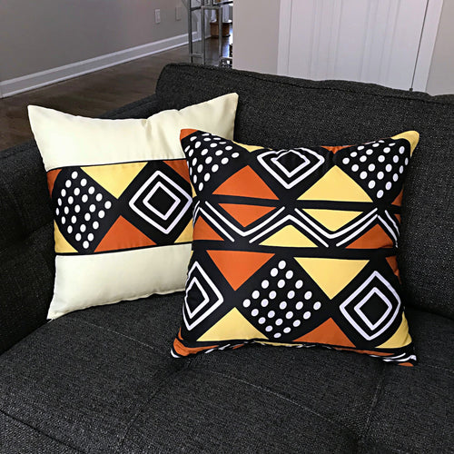 Two cream, black, orange and yellow geometric cushion covers on a dark sofa