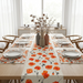 White table runner with orange and red flowers and matching placemats.