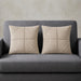 Two cream cushion covers with geometric panel stitching on a grey sofa.
