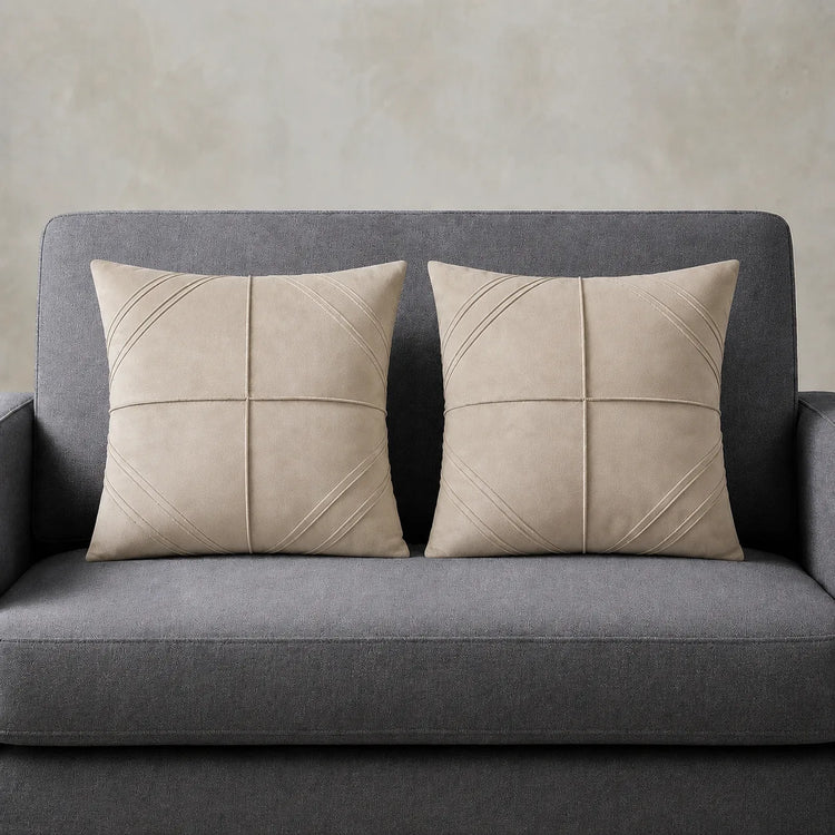 Two cream cushion covers with geometric panel stitching on a grey sofa.
