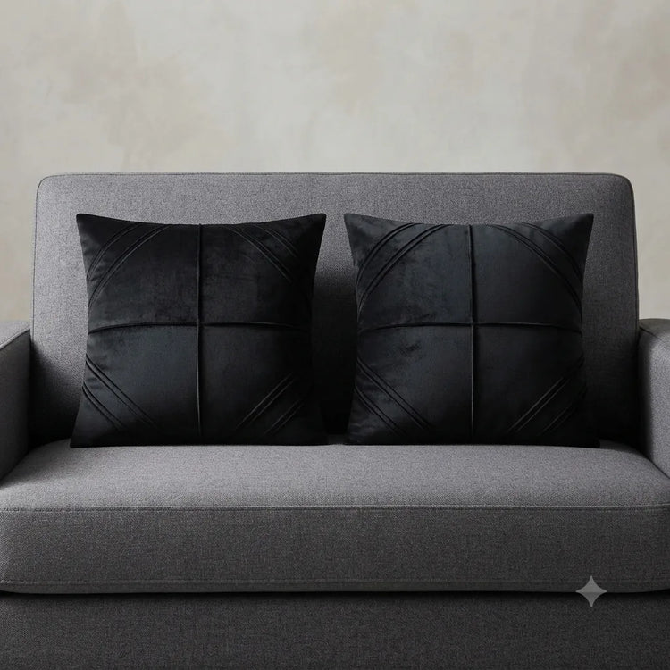Two black cushion covers with geometric panel stitching on a grey sofa.
