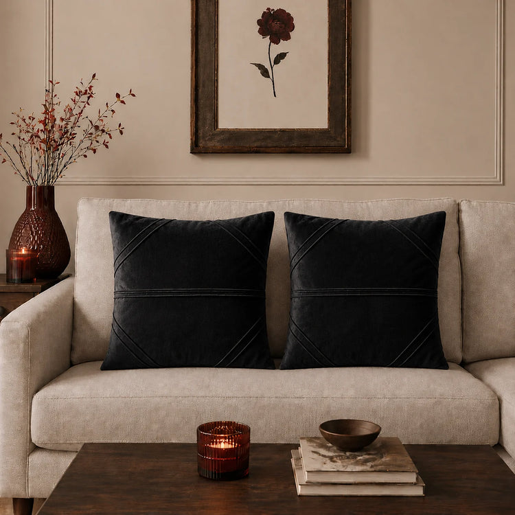 Two black cushion covers with fine horizontal stitched lines on a beige sofa.