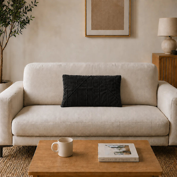 Rectangular black filled cushion with angular stitched lines on a cream sofa.