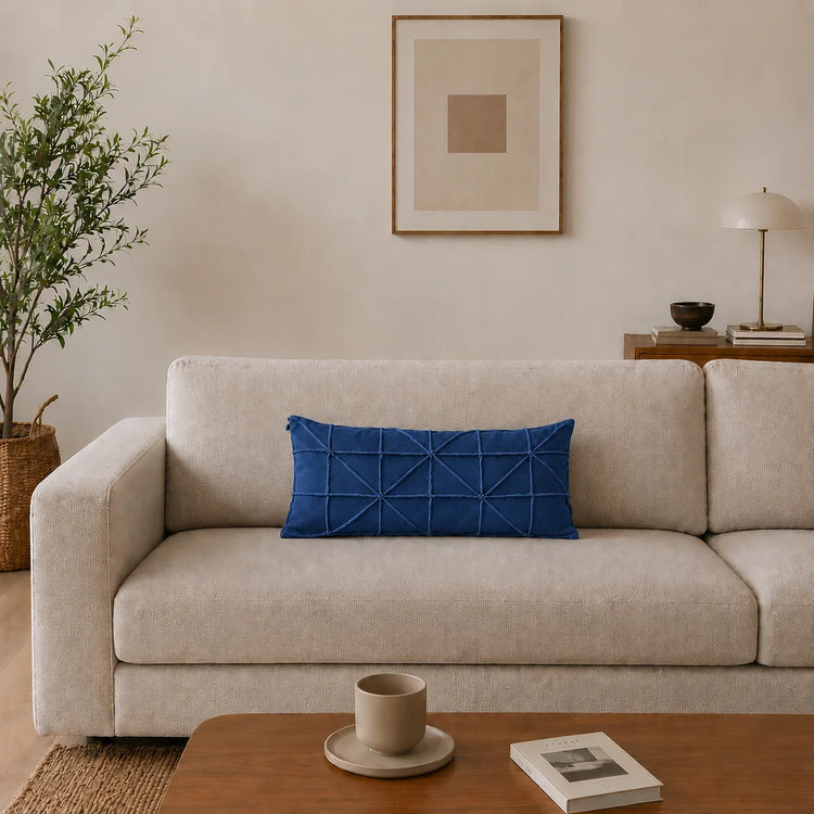 Rectangular blue filled cushion with intersecting geometric stitching on a cream sofa.