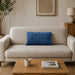 Rectangular blue filled cushion with angular stitched lines on a cream sofa.