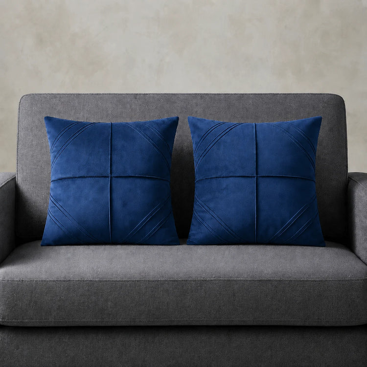 Two blue cushion covers with geometric panel stitching on a grey sofa.