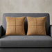 Two tan cushion covers with geometric panel stitching on a grey sofa.