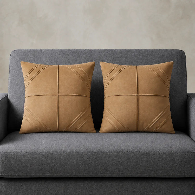 Two tan cushion covers with geometric panel stitching on a grey sofa.