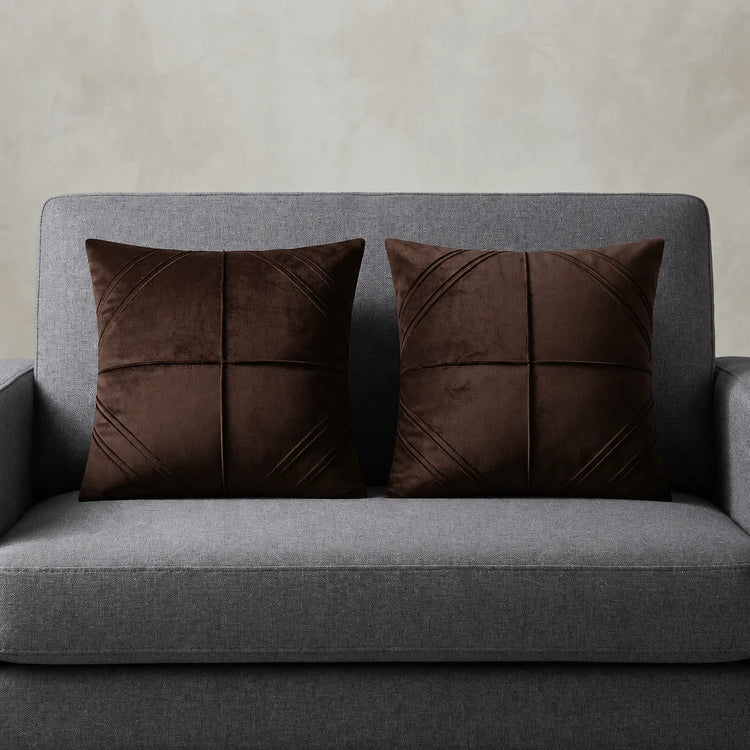 Two dark brown cushion covers with geometric panel stitching on a grey sofa.
