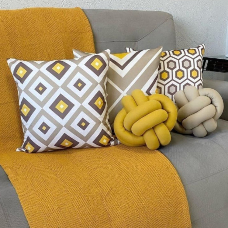 Three yellow, grey and white geometric cushion covers beside decorative knot cushions on a sofa.