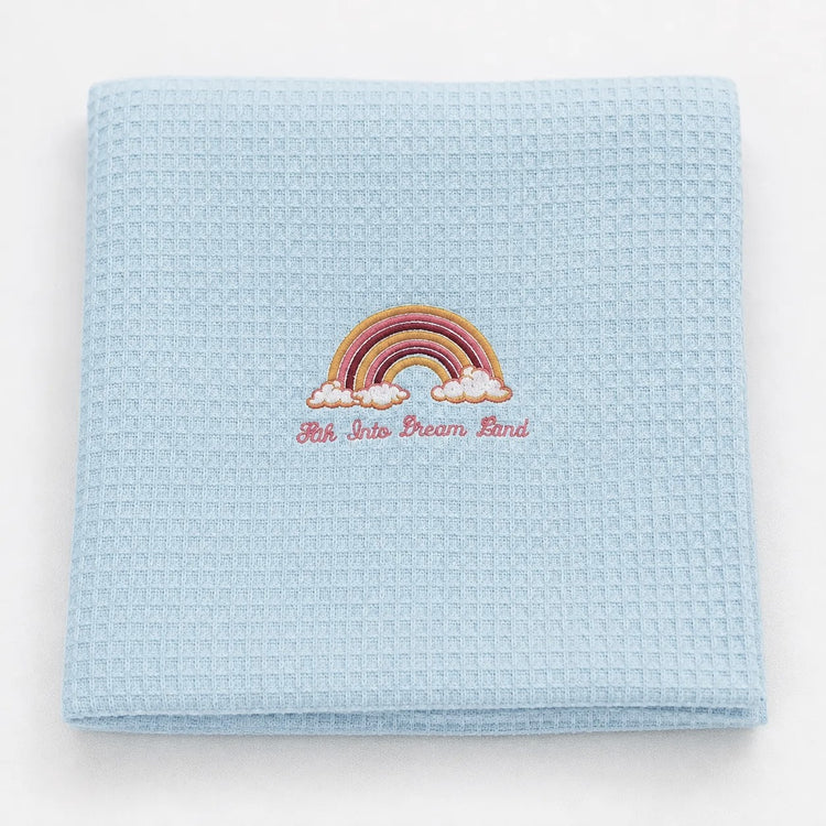 Folded pale blue waffle-weave baby blanket with a rainbow motif.