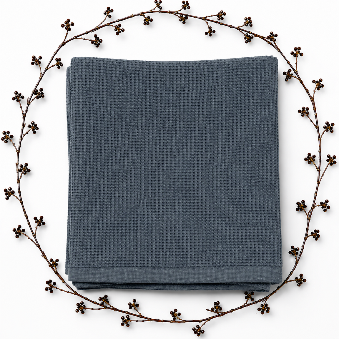 Folded dark grey waffle-textured blanket with a plain border, framed by decorative dried branches.