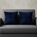 Two navy cushion covers with geometric panel stitching on a grey sofa.