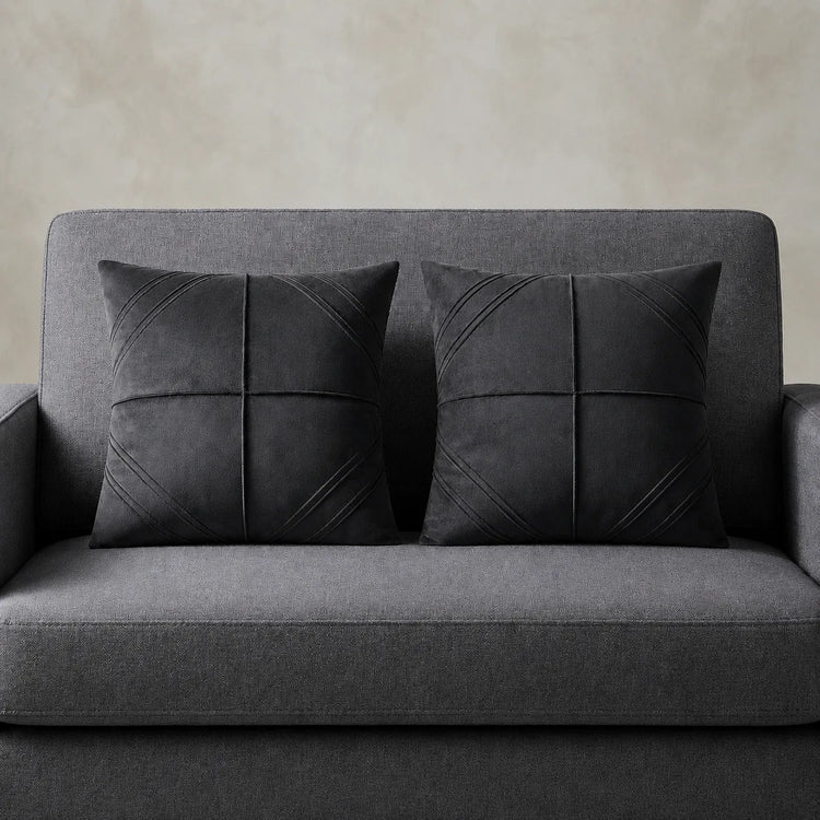 Two charcoal grey cushion covers with geometric panel stitching on a grey sofa.