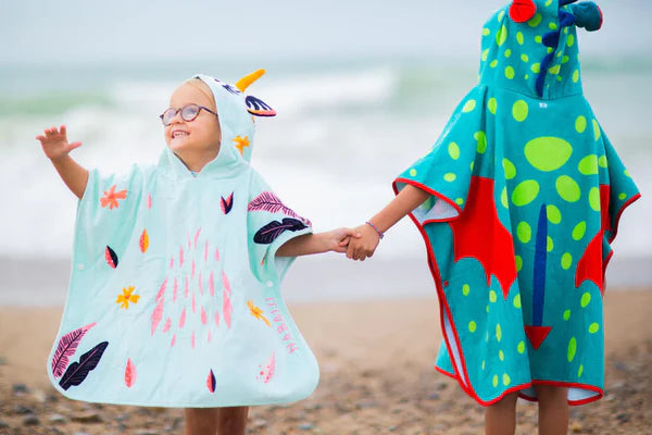 Children wearing animal-themed hooded towel ponchos at the beach.