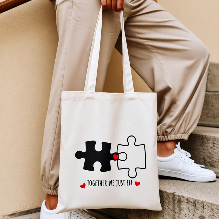 Cream tote bag with interlocking puzzle pieces and small red hearts.