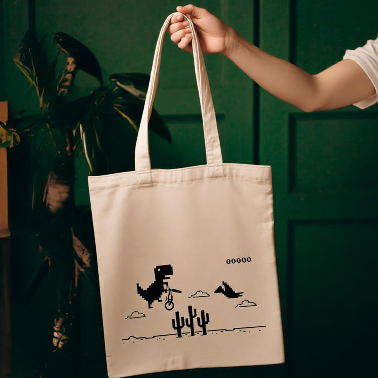 Cream tote bag with a pixel-style dinosaur and cactus print.
