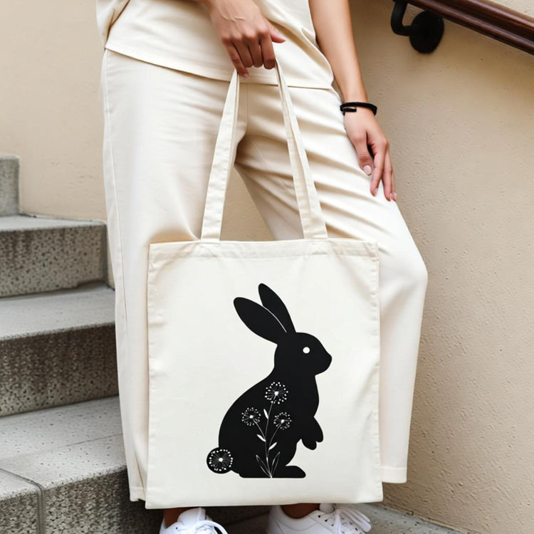 Cream tote bag with a black rabbit silhouette and small floral details.