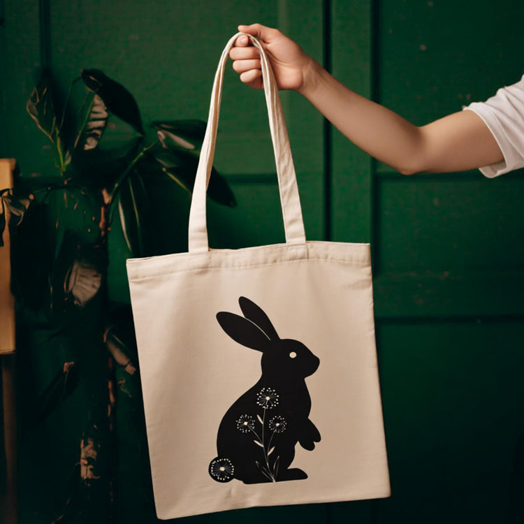 Cream tote bag with a black rabbit silhouette and small floral details.