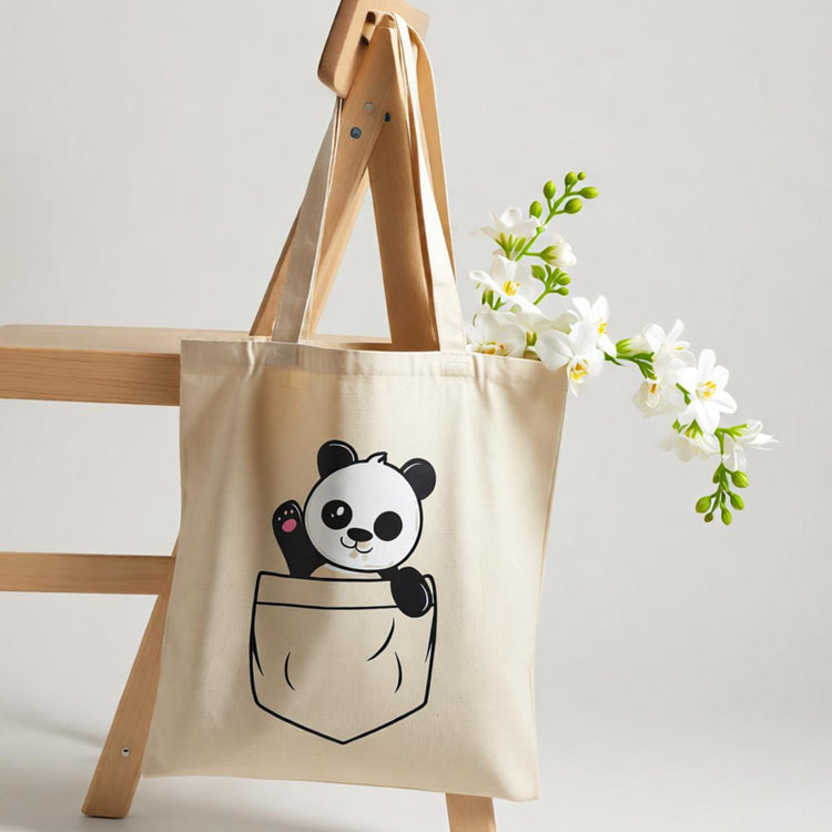 Cream tote bag with a cartoon panda peeking out of an illustrated pocket.