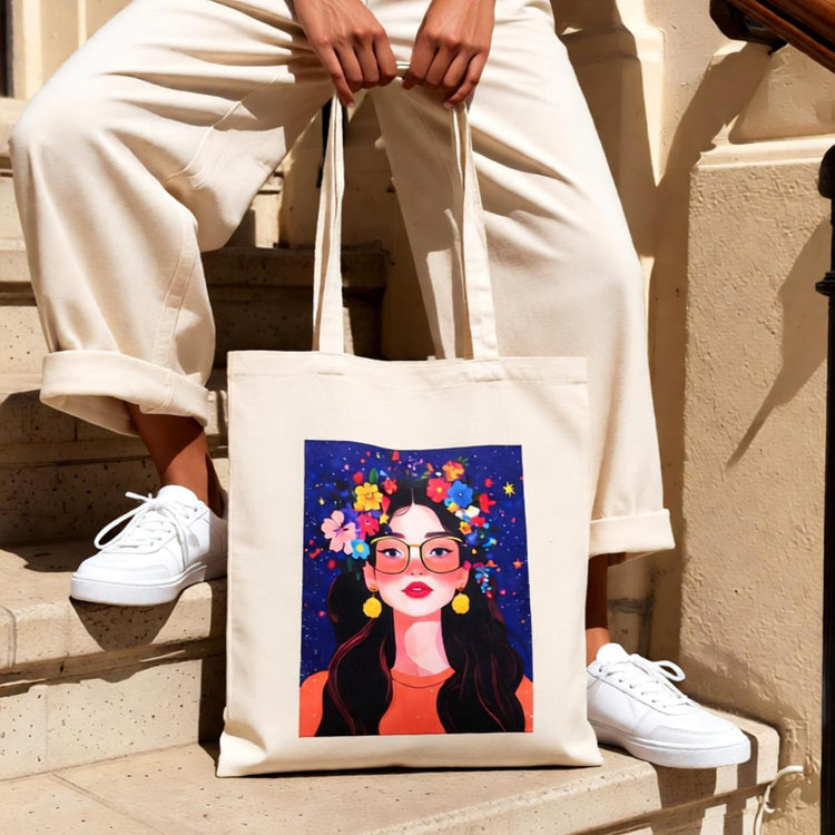 Cream tote bag with a colourful illustrated woman's portrait on a dark background.
