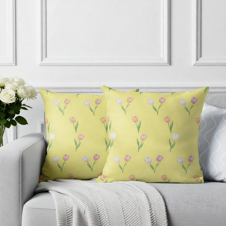 Two pale yellow cushion covers with small pink tulips on a sofa.