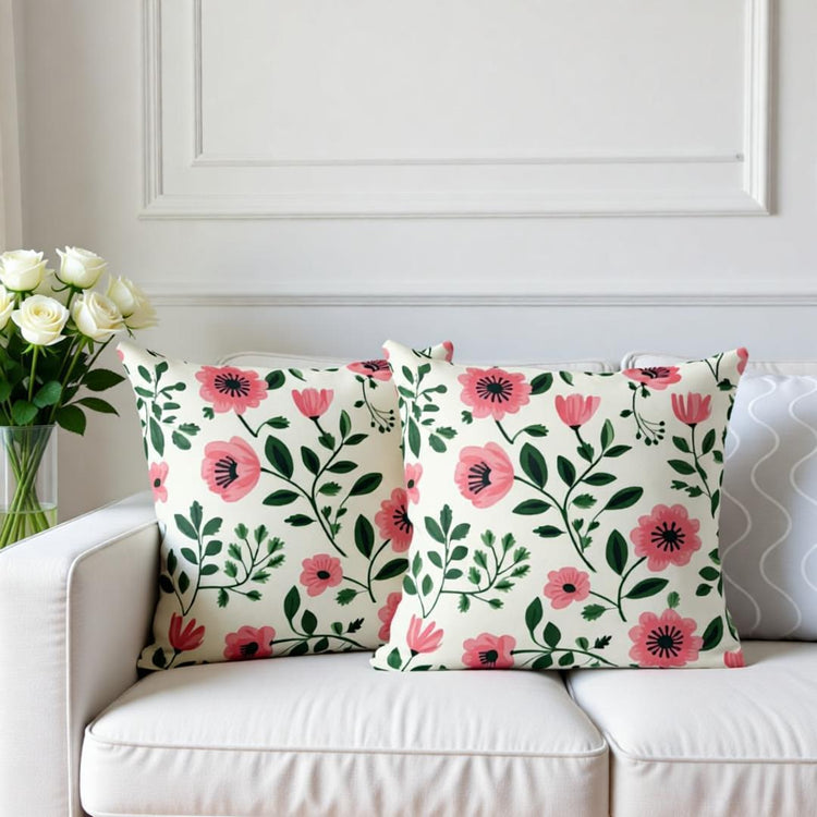 Two cream cushion covers with pink flowers and green leaves on a sofa.