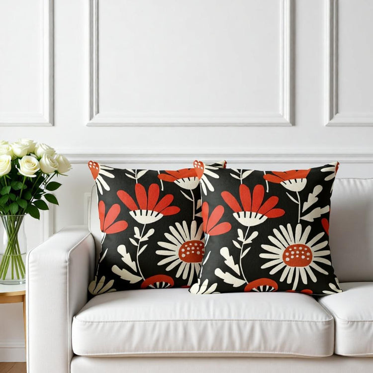 Two black cushion covers with red and cream flowers on a sofa.