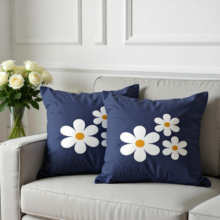 Two navy cushion covers with large white daisies on a sofa.