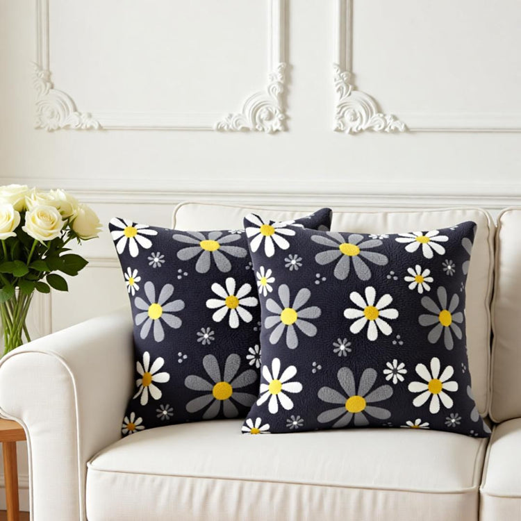 Two dark grey cushion covers with white and grey daisies on a sofa.
