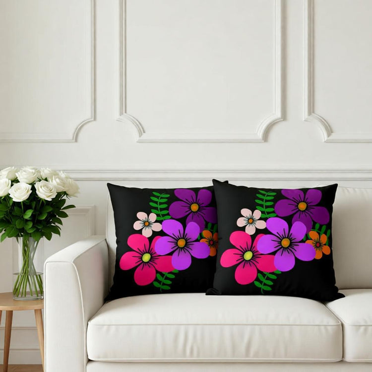 Two black cushion covers with bold pink and purple flowers on a white sofa.