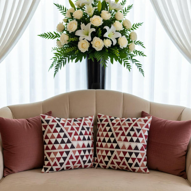 Two small-triangle patterned cushion covers in red, black and cream on a burgundy sofa.
