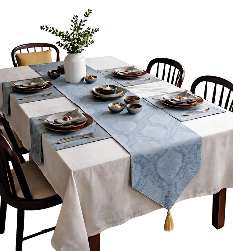 Blue ornamental table runner with matching mats over a white tablecloth.