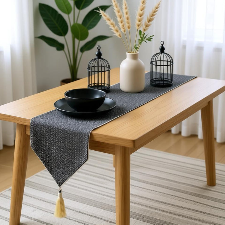 Black textured table runner with a pointed tasselled end on a wooden table.