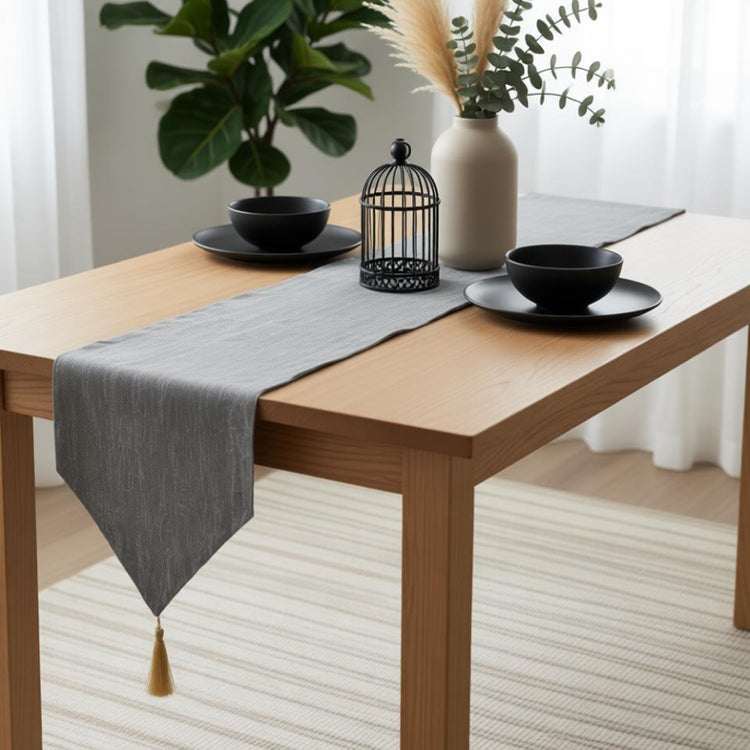 Grey table runner with a pointed end and gold-coloured tassel.