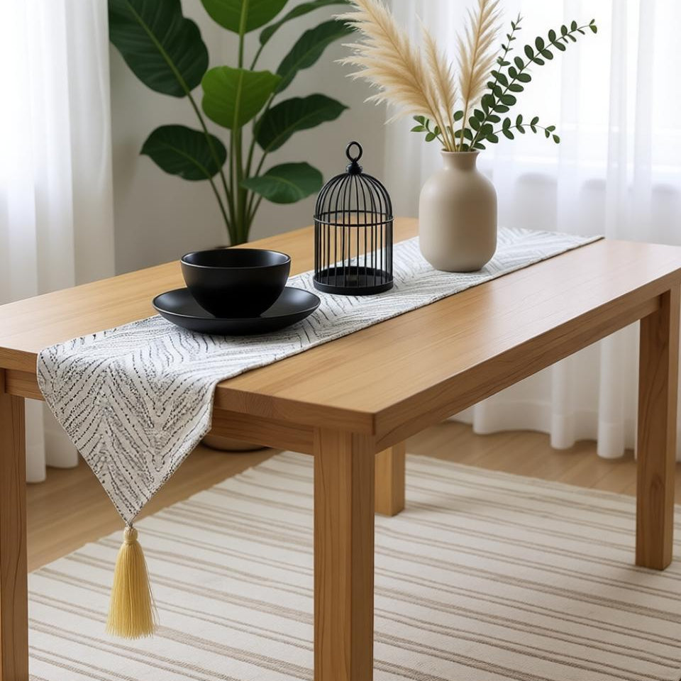 Silver chevron-pattern table runner with a tasselled end on a wooden table.