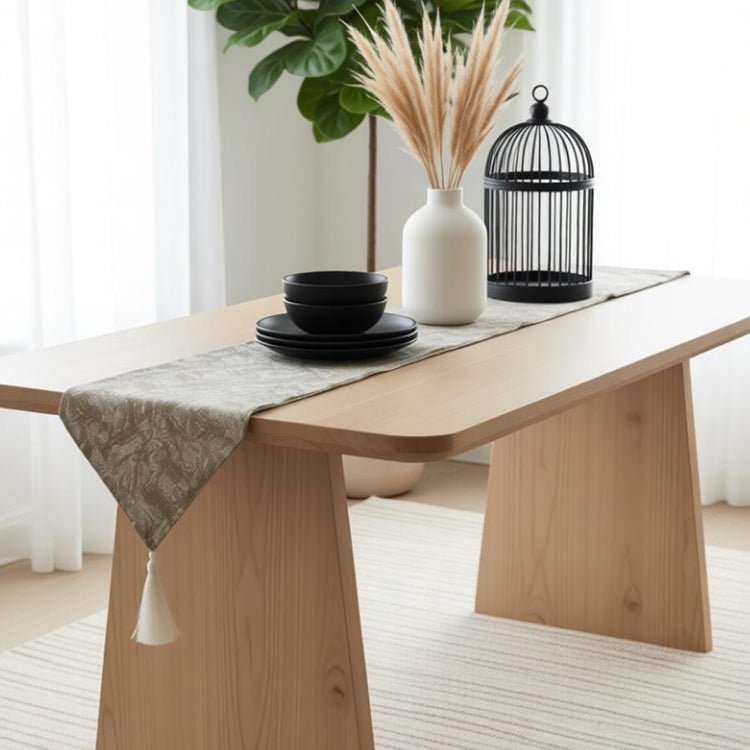 Grey ornamental table runner draped over a wooden table with black crockery.