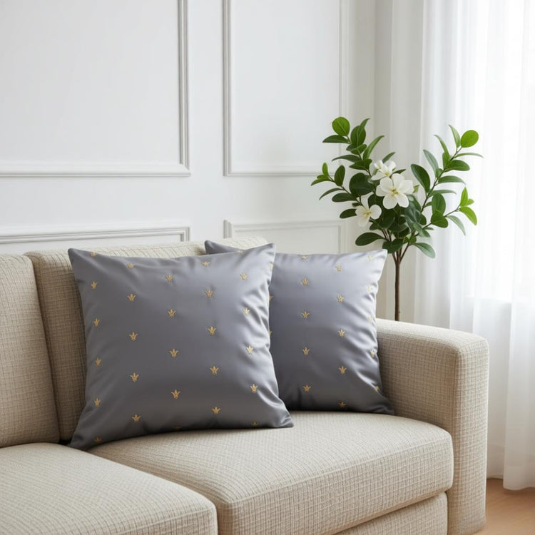 Two grey cushion covers with small gold coloured motifs on a cream armchair.