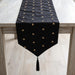 Black velvet table runner with small gold-coloured motifs and a tasselled point.