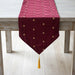 Burgundy velvet table runner with small gold-coloured motifs and a tasselled point.