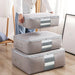 Grey zippered clothes-storage bags stacked beside a person holding one bag.