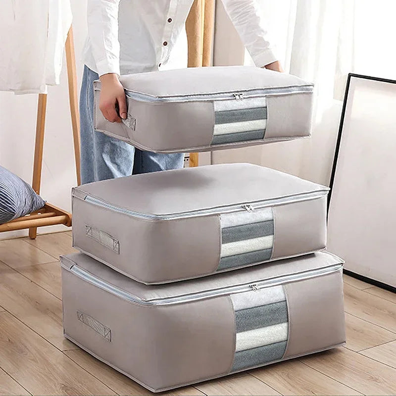 Grey zippered clothes-storage bags stacked beside a person holding one bag.